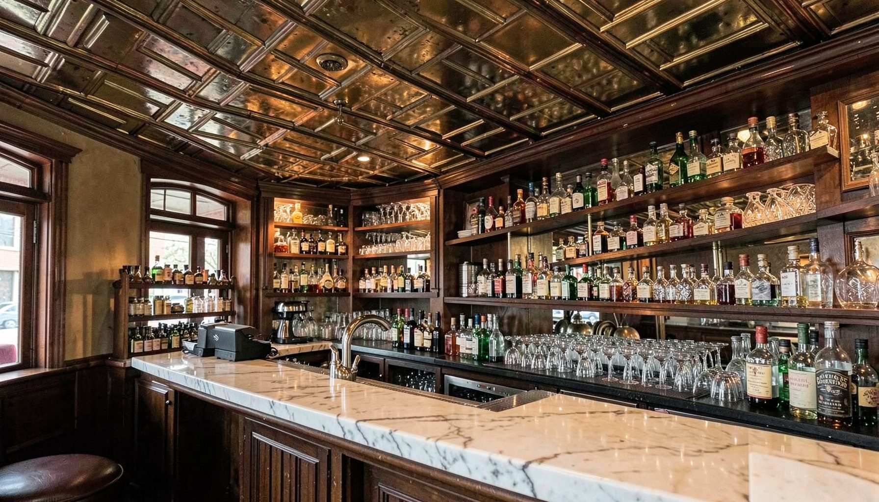 Cozy Capitol Hill bar interior with vintage tin ceiling, marble counter, and shelves of bitters and glassware