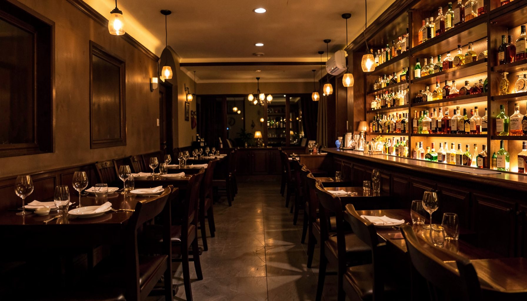 Elegant Indian restaurant dining room with dark wood tables, amber lighting, and a long bar