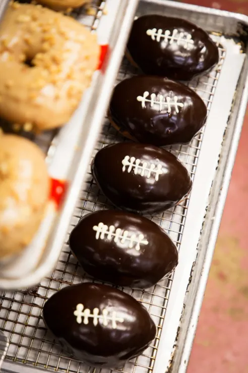 Close-up of football-shaped chocolate-glazed pastries with white icing laces resting on a metal cooling rack